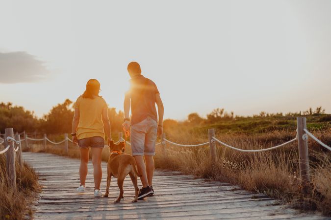 Casual adult couple walking with dog along rural pathway
