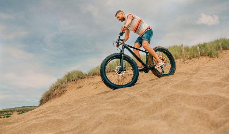 Male riding bicycle down sandy dune