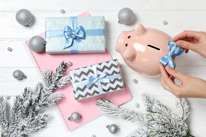 Piggy bank, notepad, gift boxes and hands on neutral wooden background, top view