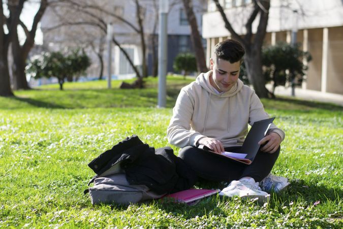 Young man sitting on the school grass while reading a book