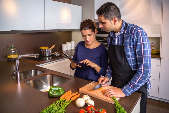 Couple checking digital tablet while prepping vegetables for dinner