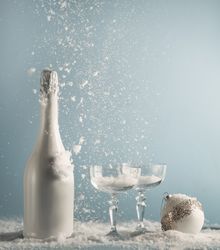 champagne bottle and glasses with Christmas bauble on table with snowfall at blue wall background