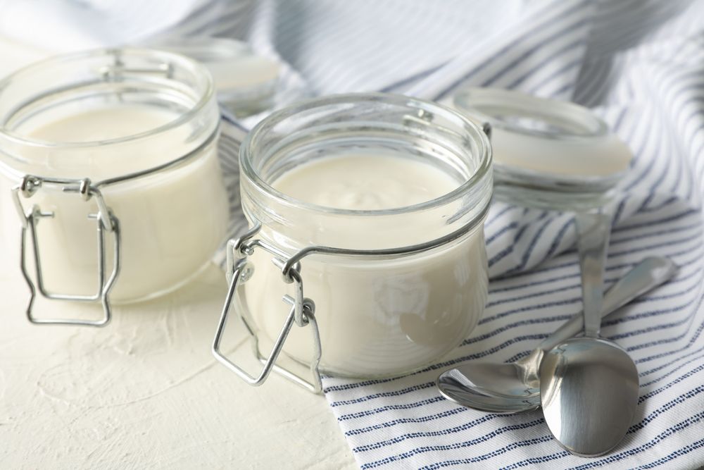 Glass jars with sour cream yogurt, spoons and towel on cement background