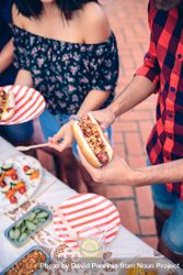 Man in red plaid holding hot dog at barbecue with friends 4OddqR