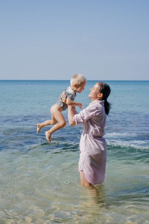 Woman and small kid having fun with water while relaxing on seacoast at resort