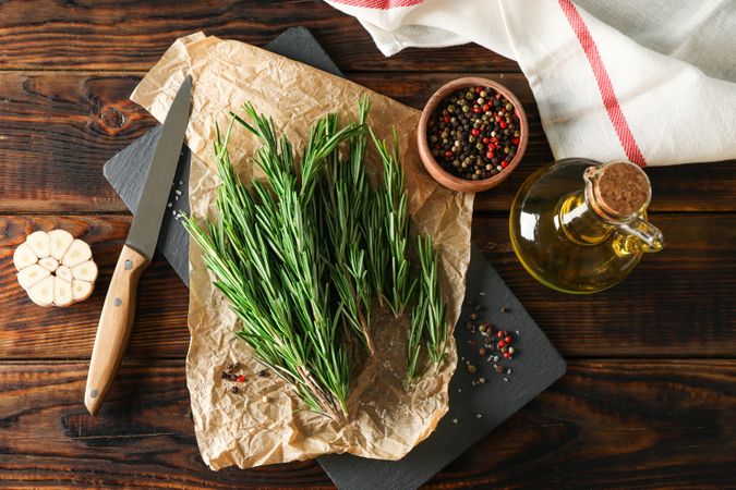 Composition with rosemary, oil, pepper, garlic and knife on wooden table, top view