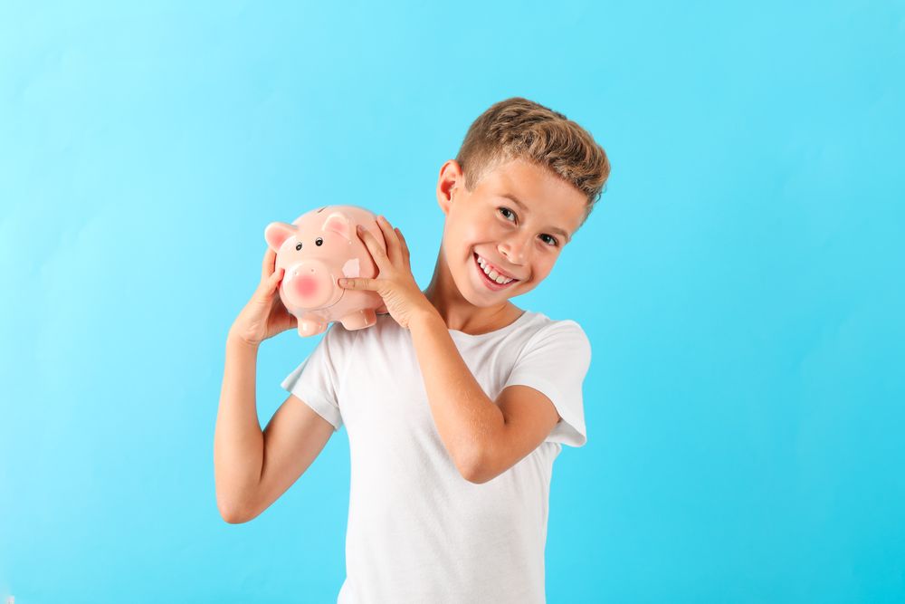 Boy with piggy bank against color background, space for text