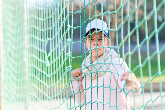 Portrait of a teenage male wearing a cap behind sports net