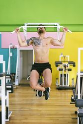 Front of man working out shoulders in a fitness club on pull up bar
