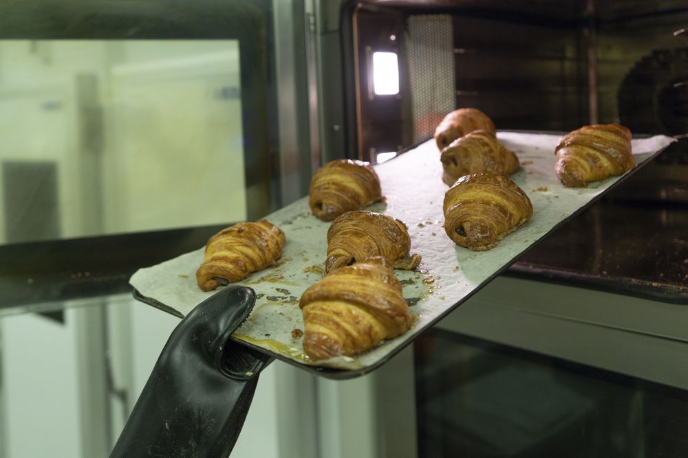 Cook holding baking tray with hot croissants