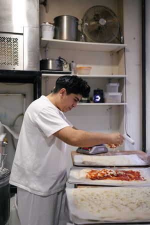 Young baker putting ingredients in pizza
