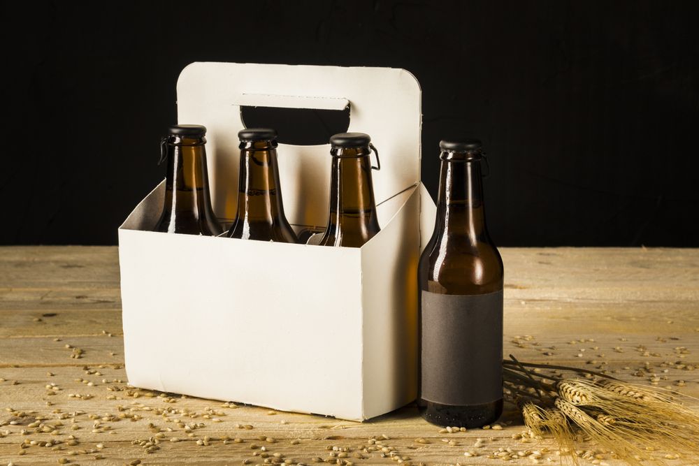 Beer bottles in carton box and ears of wheat on wooden surface