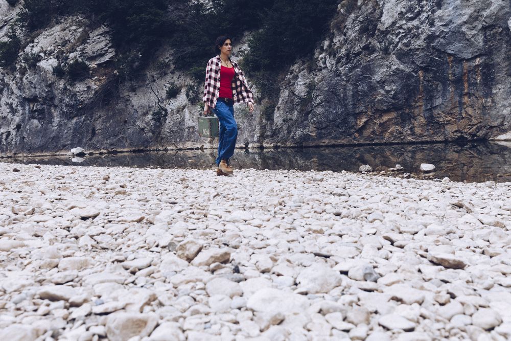 Woman with case walking on shore above stream