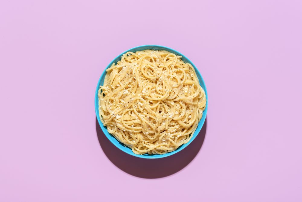 Spaghetti with cheese and black pepper, top view on a purple background