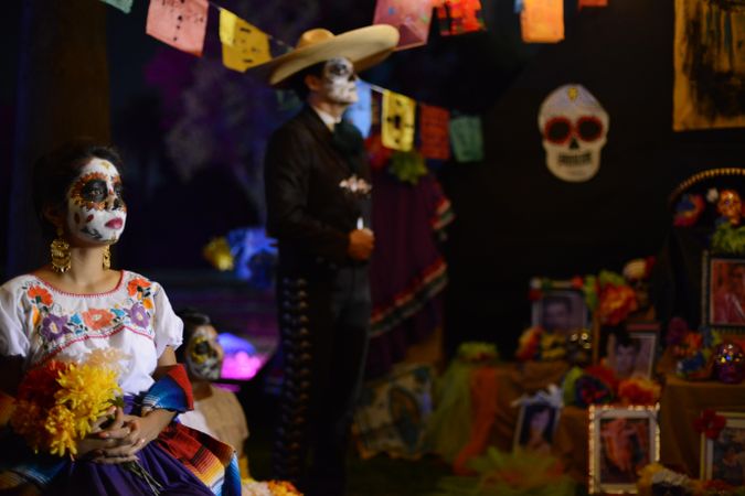 Woman in traditional Dia de Los Muertos attire sitting at altar