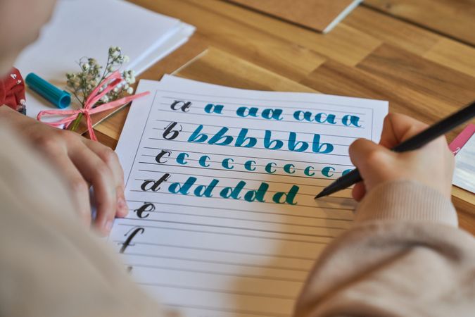 Crop person drawing letters on paper sheet