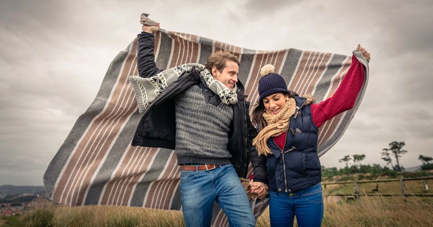 Portrait of cute couple playing outdoors with blanket on a windy day over dark cloudy sky