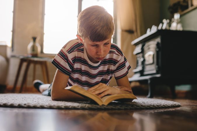 Boy relaxing on a carpet and reading a book at home