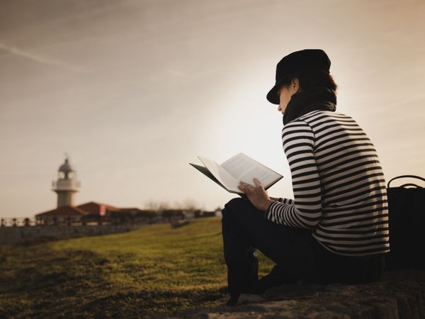 Woman with book on grass near lighthouse