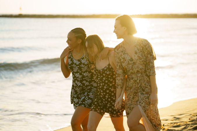 Three happy women skipping towards the coast on beach with their arms around each other