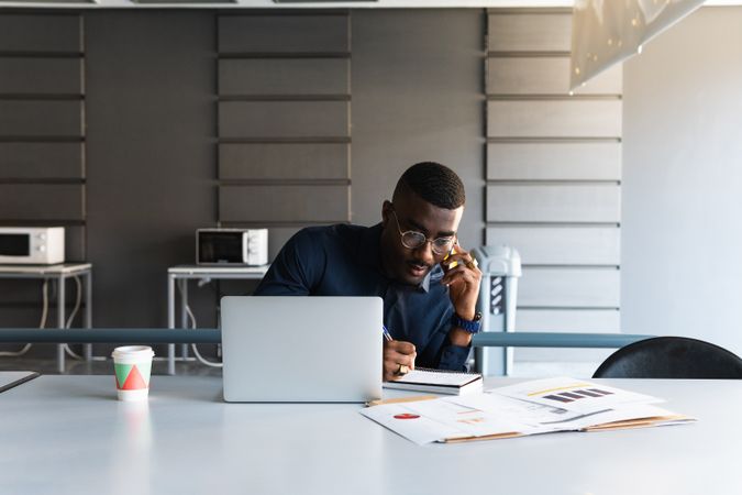 Black man talking on phone near laptop in office
