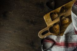 Heart shaped cookie cutters on wooden cutting board with kitchen towel with copy space