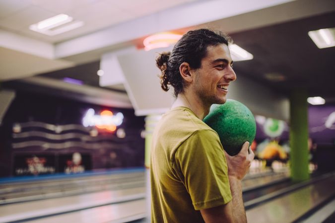 Happy man holding bowling ball and preparing to bowl down the lane