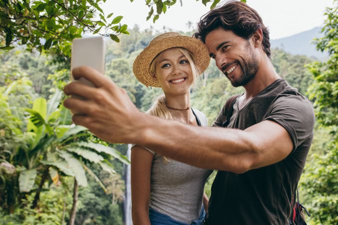 Smiling young couple taking selfie with waterfall in background