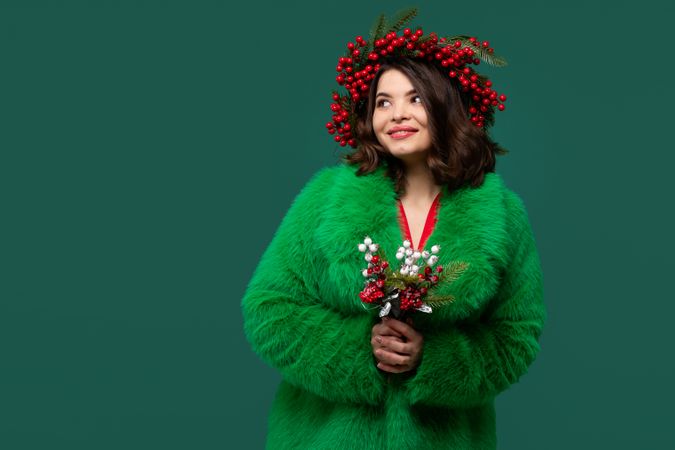 Woman in coat and red berry wreath gazes upward thoughtfully.