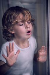 Calm kid blowing on window glass at home