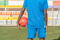 Black football player with ball standing on stadium