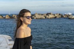 Happy woman with long hair standing on the coast and smiling, side view