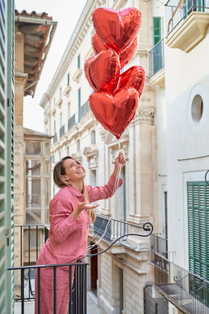 Positive female with red balloons on balcony of multistory build