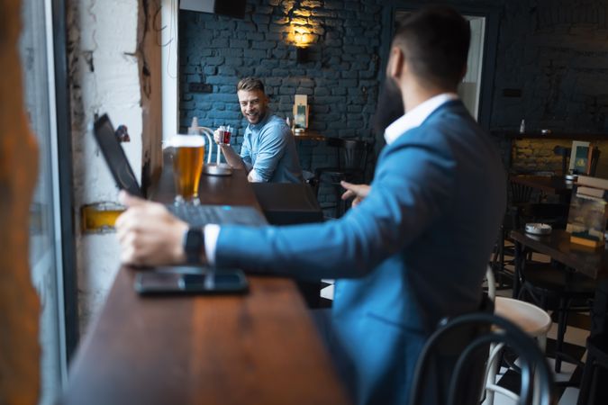 Man with laptop and beer turning to speak to another patron