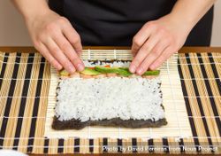 Hands of woman chef arranging filling in rice to roll sushi in a nori seaweed sheet 4ABOzb