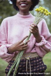 Woman in pink sweater holding yellow flower 5qLBp0