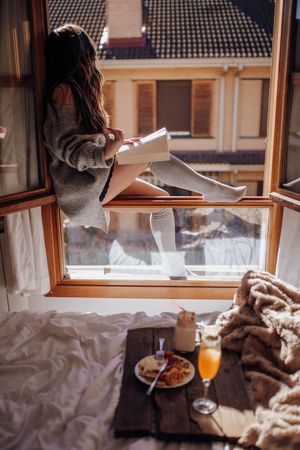 Young woman sitting with tasty drink and book on window