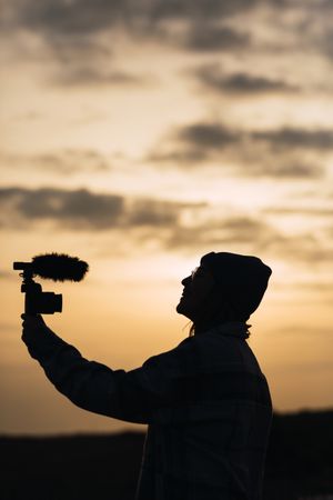 Anonymous happy woman recording vlog on camera under sundown sky