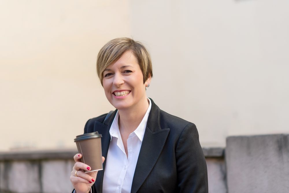 Happy female in blazer sitting outside with coffee