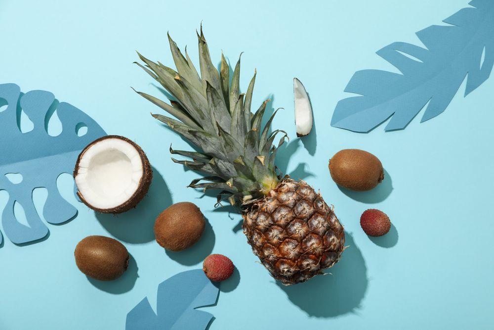 Set of tropical fruit and paper tropical leaves on blue background, top view