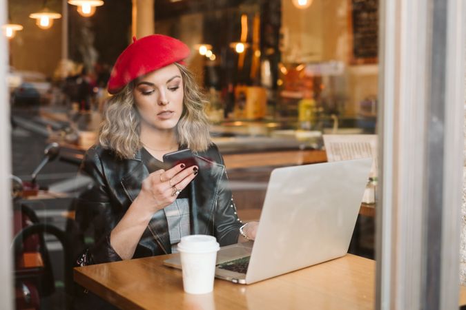 Woman with laptop using smartphone in cafe