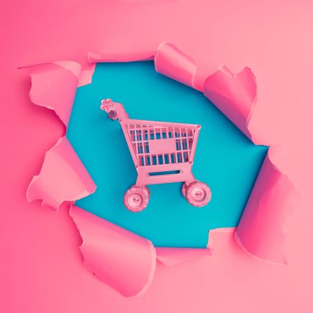 Torn pink paper revealing shopping cart underneath on blue background
