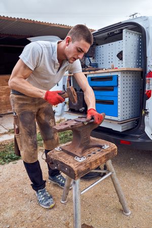 Blacksmith working on the anvil changing the horseshoe to a paw with tools