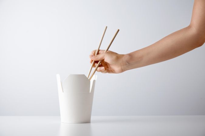 A person reaching into a to go container with chopsticks