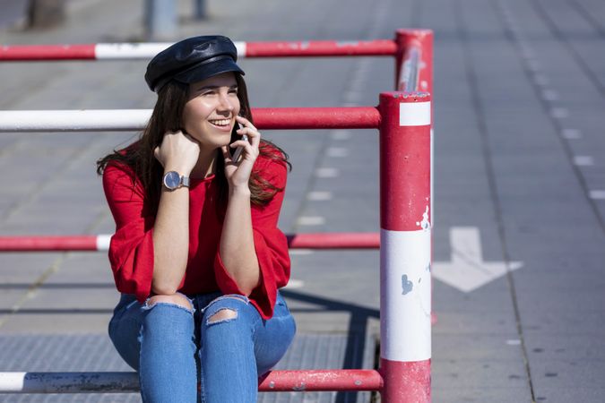 Beautiful young woman sitting on a metallic rail while using a mobile phone outdoors in the street in a bright day