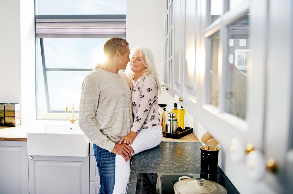 Grey haired woman sitting on kitchen counter with her husband