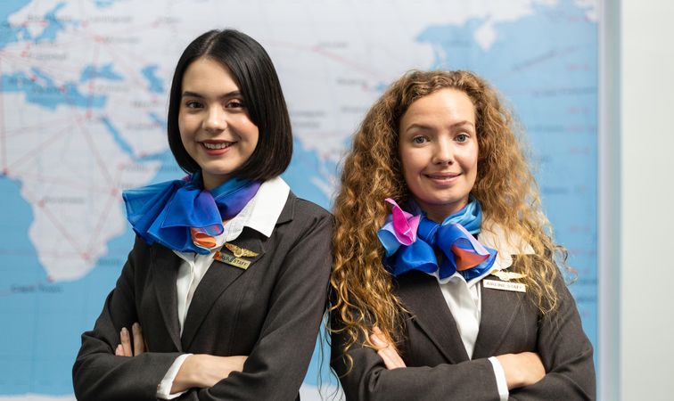Two flight attendants in uniforms posing in front of world map