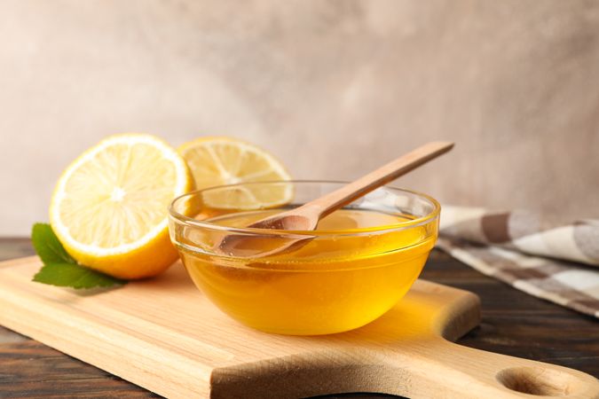 Lemons and bowl with honey and dipper on wooden background, space for text