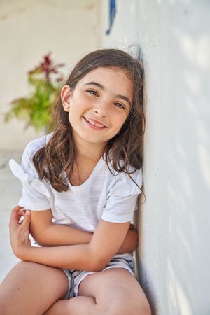 Smiling girl sitting on sidewalk near wall