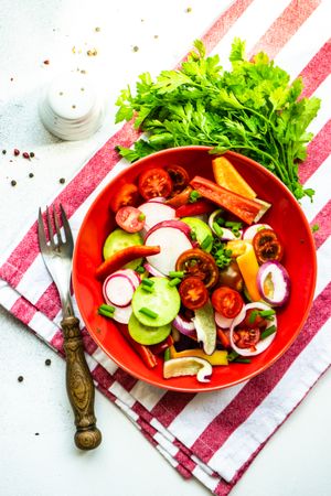 Top view of colorful healthy raw vegetable salad served in red bowl on red striped napkin
